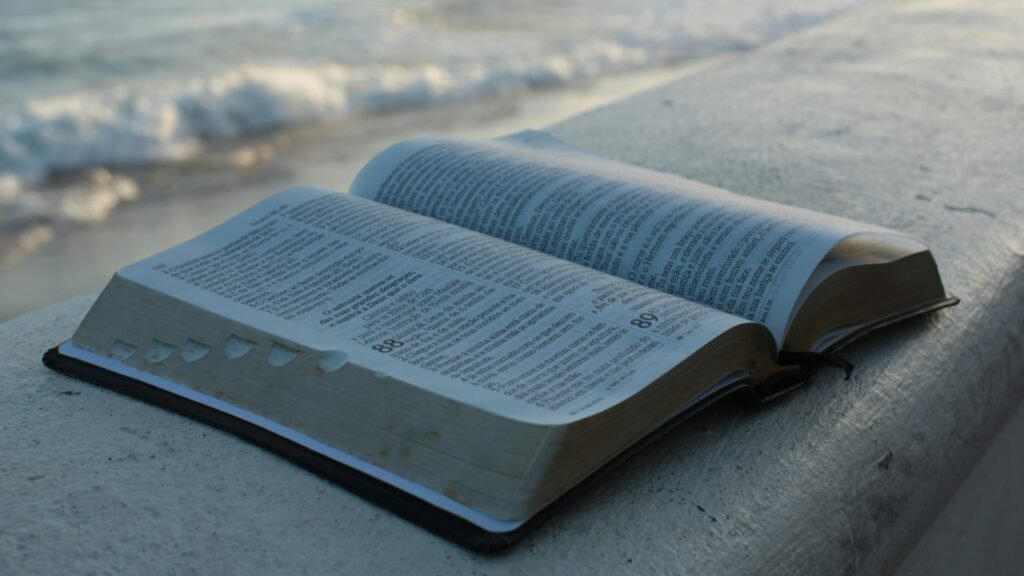 pexels-photo-13011292-13011292 An open Bible on a concrete surface by the beach, evoking peace and reflection.